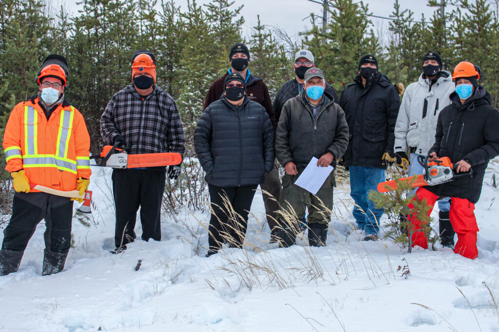 A group of Participants in the Lynn Lake Youth Development Program standing outside in the snow wearing protective equipment and tools.